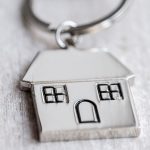 House key and keychain in the form of homes lies on wooden boards. Concept for real estate, mortgage, moving home or renting property.