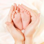 Baby Newborn Feet in Mother Hands. Beautiful New Born Kid Foot,