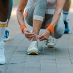 cropped view of senior woman sitting and tying shoelaces in park