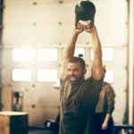 Smiling young man swinging a dumbbell while working out