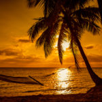 Silhouette of hammock and palm trees on a tropical beach at suns