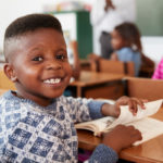 Boy at desk smiling to camera in an elementary school lesson