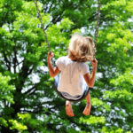 7796797 – little girl swinging on a sunny day with trees in the background