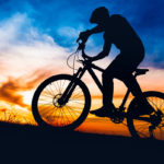 Man on mountain bike at sunset, riding bicycle on hills