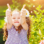 Laughing girl with daisy in her hairs, showing thumbs up.