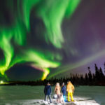 Company of friends looks northern lights at edge forest